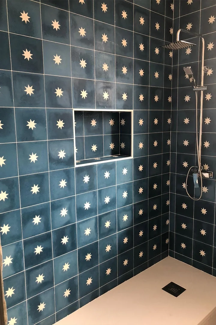 Ducha revestida con baldosas para pared de baño en color azul intenso con decoración de estrellas blancas. Un revestimiento cerámico de inspiración artesanal que convierte la zona de ducha en el principal elemento decorativo del baño.