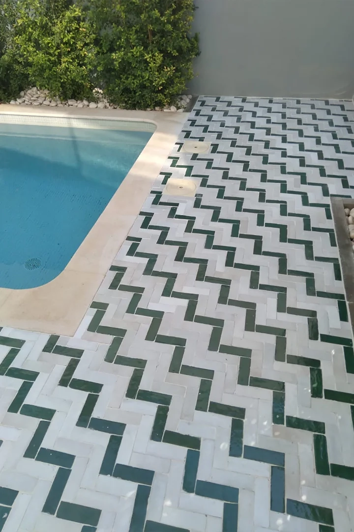 Pavimento exterior de baldosas rectangulares verdes y blancas junto a una piscina